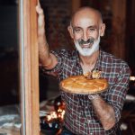 Mann lächelt und hält einen Kuchen in der Hand